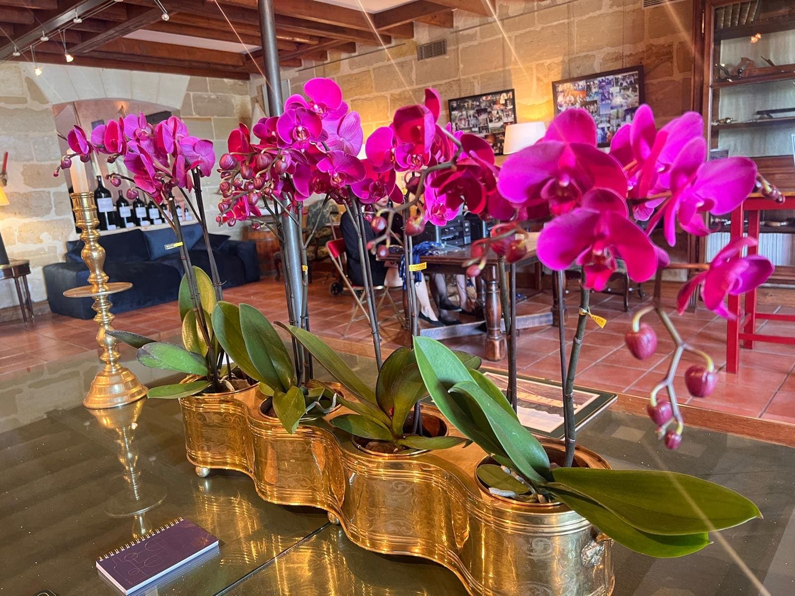 Bouquet d’orchidées roses dans des vases dorés, sur une table de dégustation aux murs en pierre