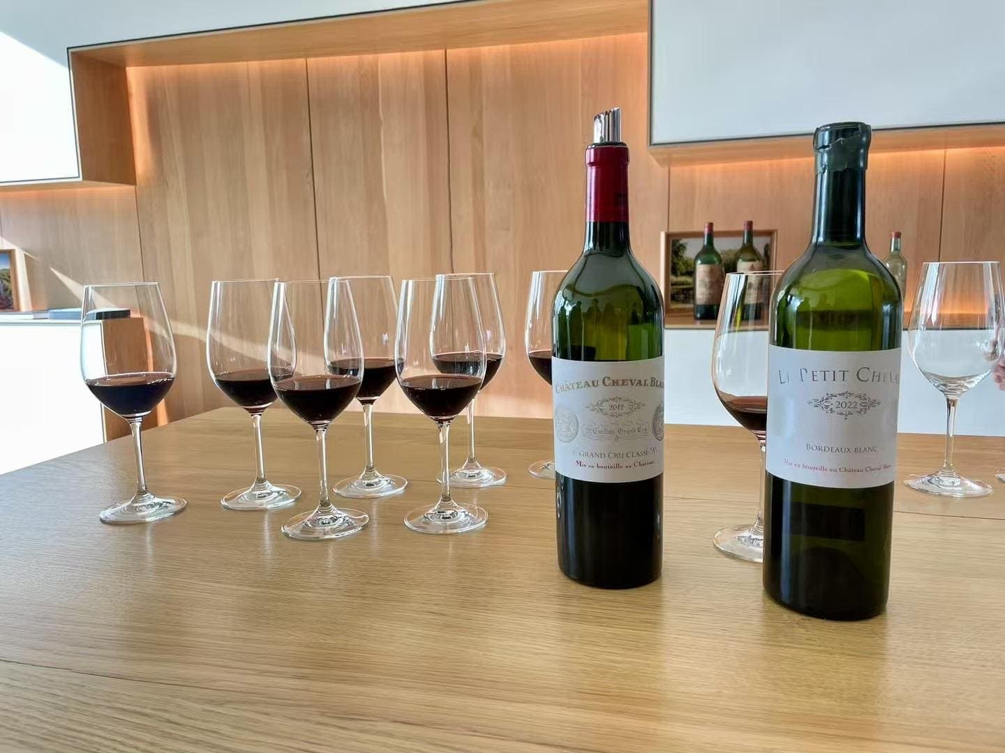 Bouteilles de Château Cheval Blanc et de Petit Cheval, verres de dégustation alignés sur un comptoir en bois