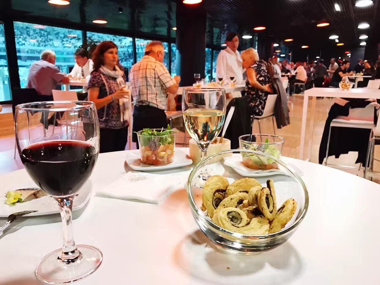 Table haute avec vin et amuse-bouches, salon de réception surplombant des gradins de stade
