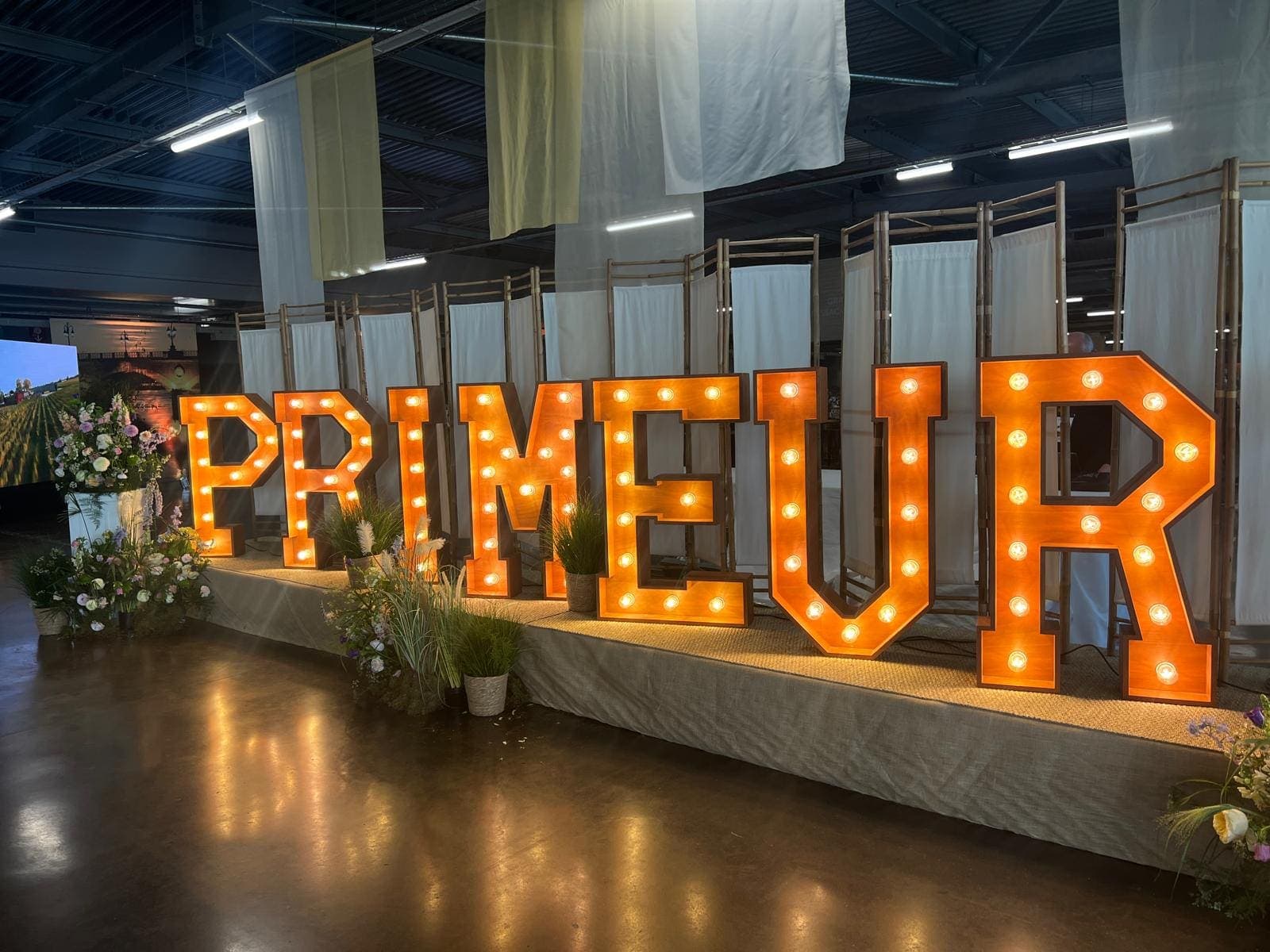 Lettres lumineuses géantes formant le mot PRIMEUR, décor floral, lors d’un salon des vins