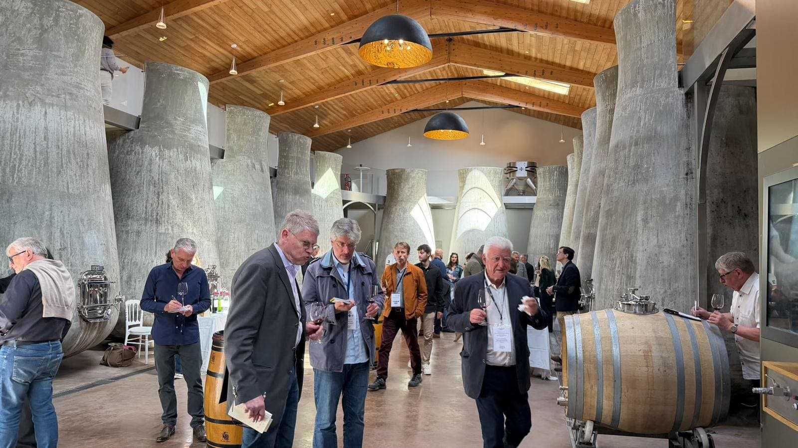 Invités circulant entre de grandes cuves coniques en béton, lors d’un événement dans un chai contemporain