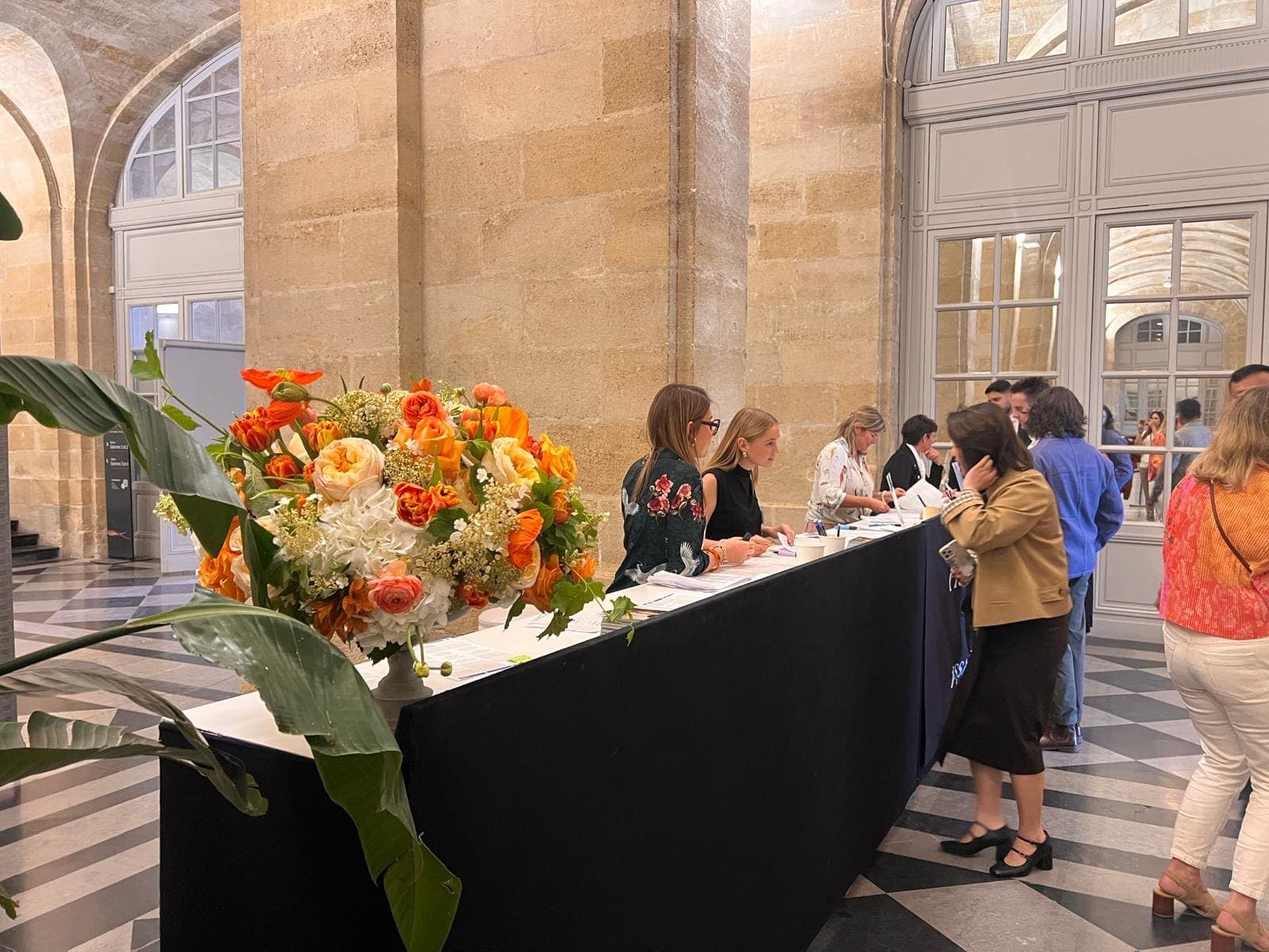Comptoir d’accueil d’un salon professionnel, grand bouquet orangé, hôtesses enregistrant les visiteurs