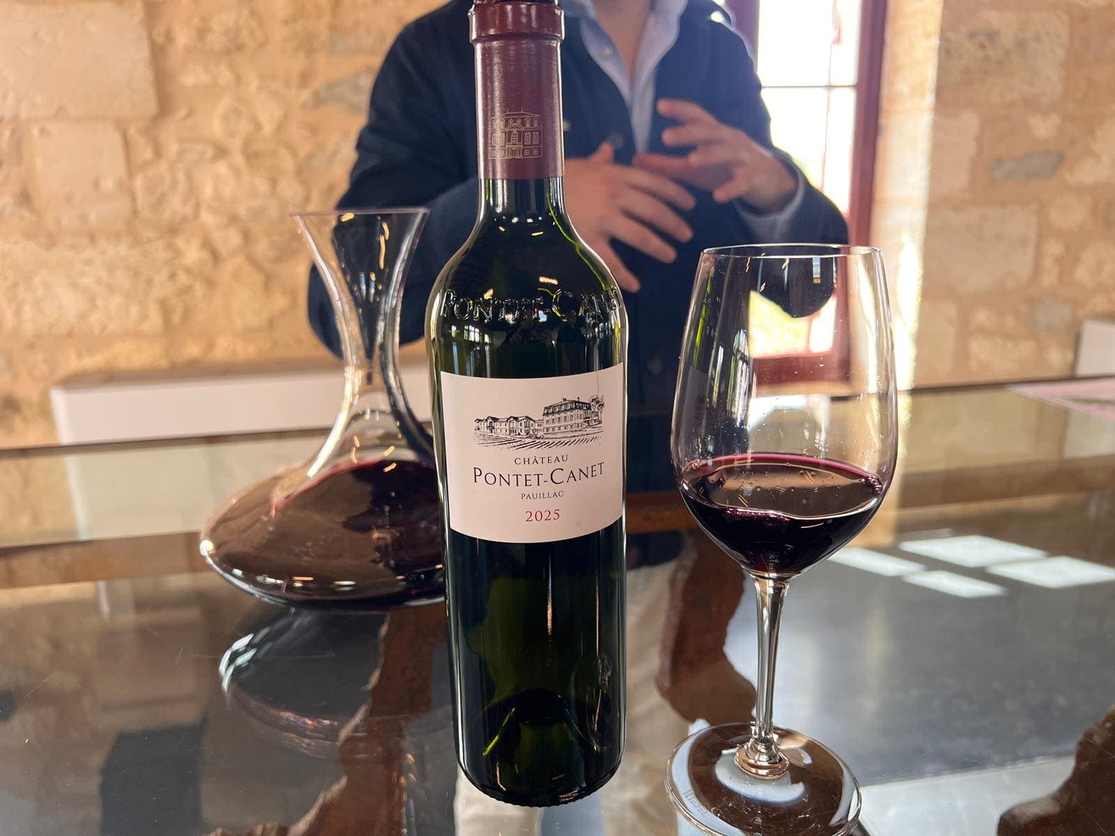 Bouteille de Château Pontet-Canet 2025, carafe et verre de vin rouge sur une table en verre