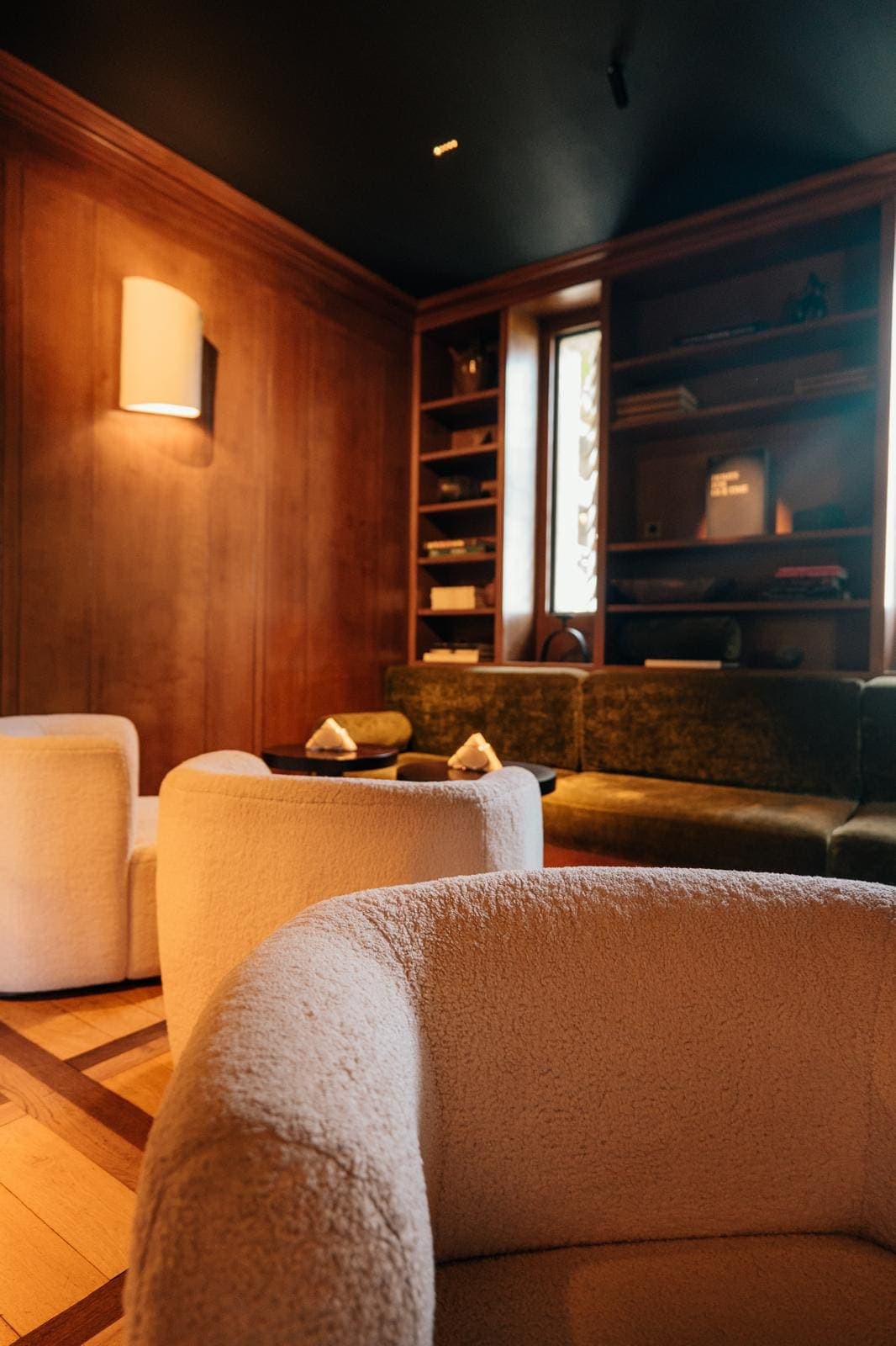 Salon cosy aux boiseries sombres, fauteuils en bouclé crème et bibliothèque garnie