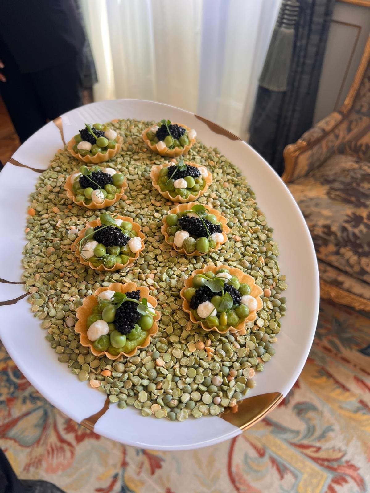 Plateau de tartelettes aux petits pois et caviar, présenté sur un lit de lentilles, dans un salon de château
