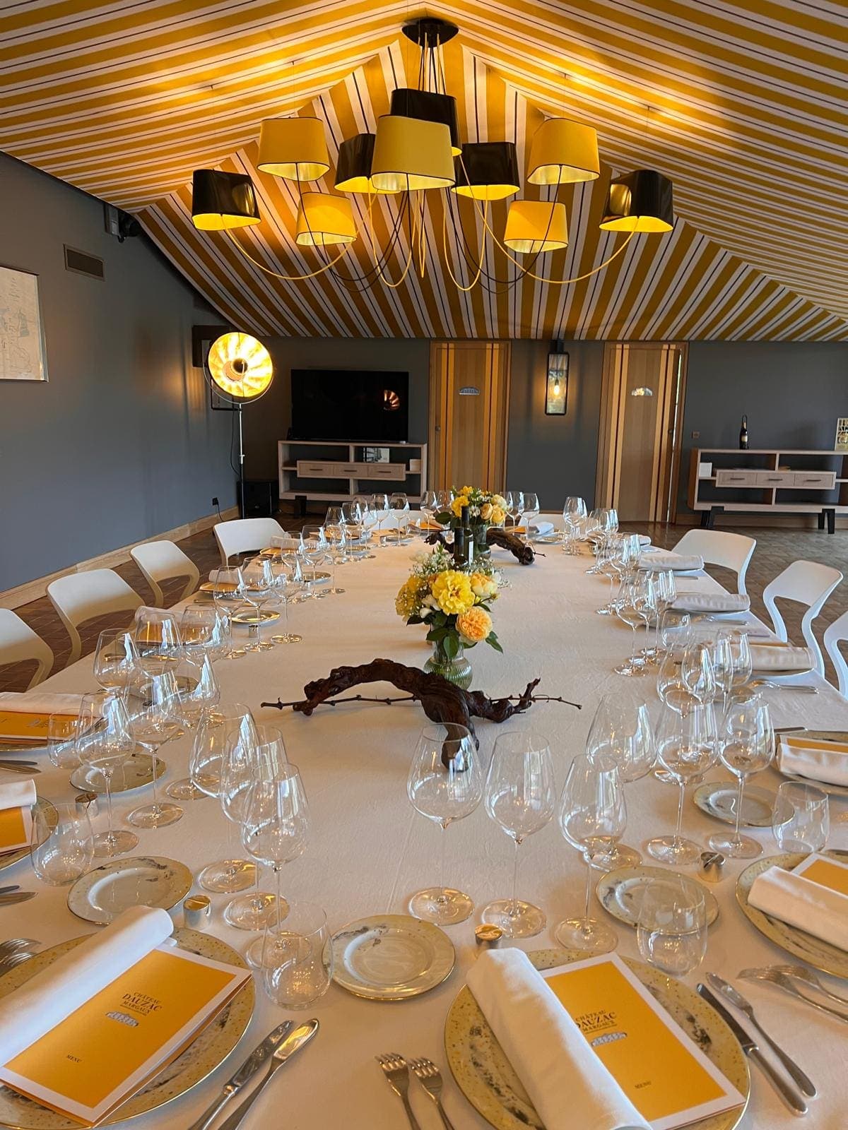 Longue table dressée sous une tente à rayures jaunes, verres alignés et centre de table floral