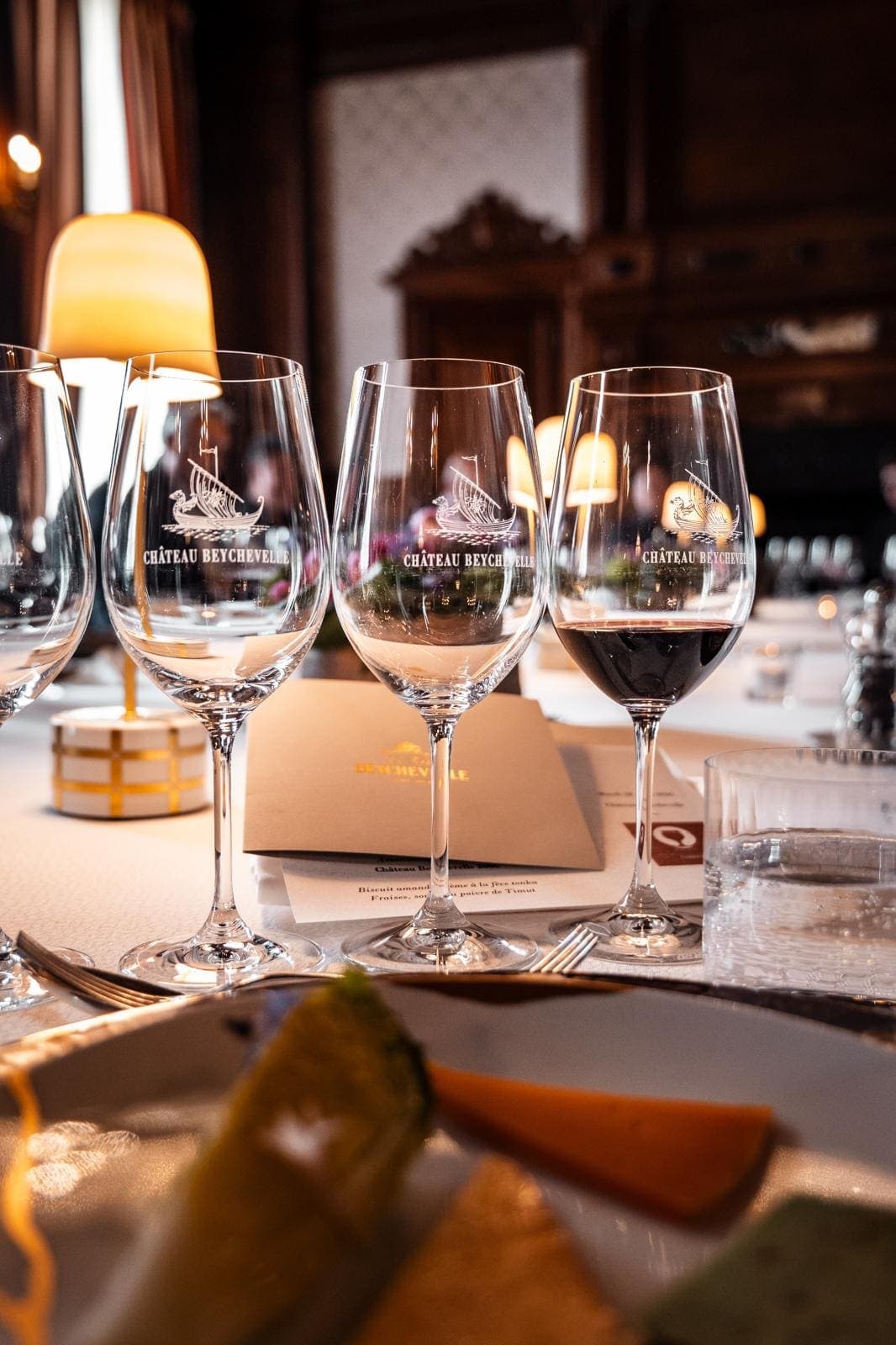 Verres gravés au nom du Château Beychevelle sur une table dressée, éclairage chaleureux