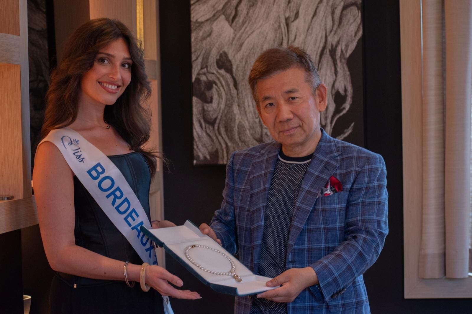 Miss Bordeaux, écharpe portée, reçoit un écrin de bijoux des mains d’un partenaire