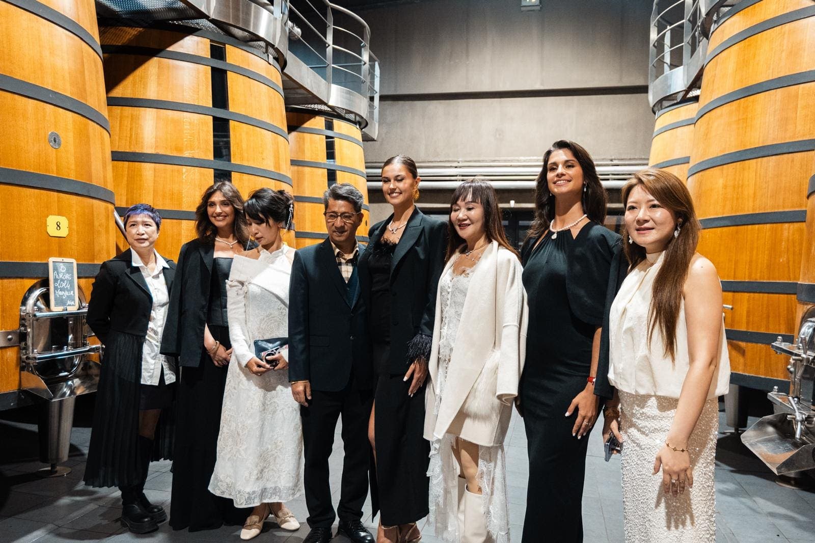 Groupe en tenue de soirée posant entre de grandes cuves en bois, lors d’une réception de gala au chai